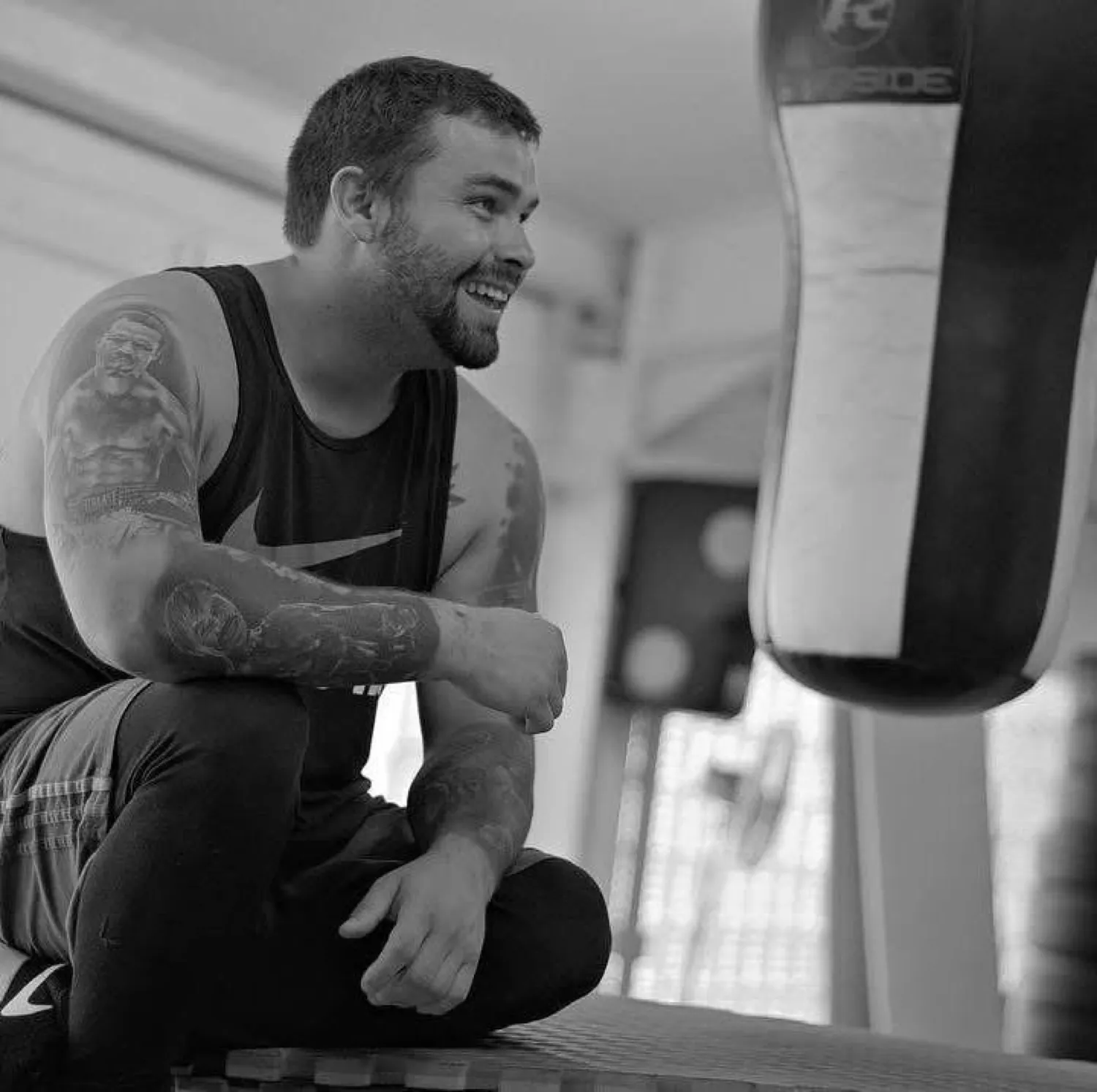 Black and white portrait of Marlee Dann sitting by a heavy bag in the gym