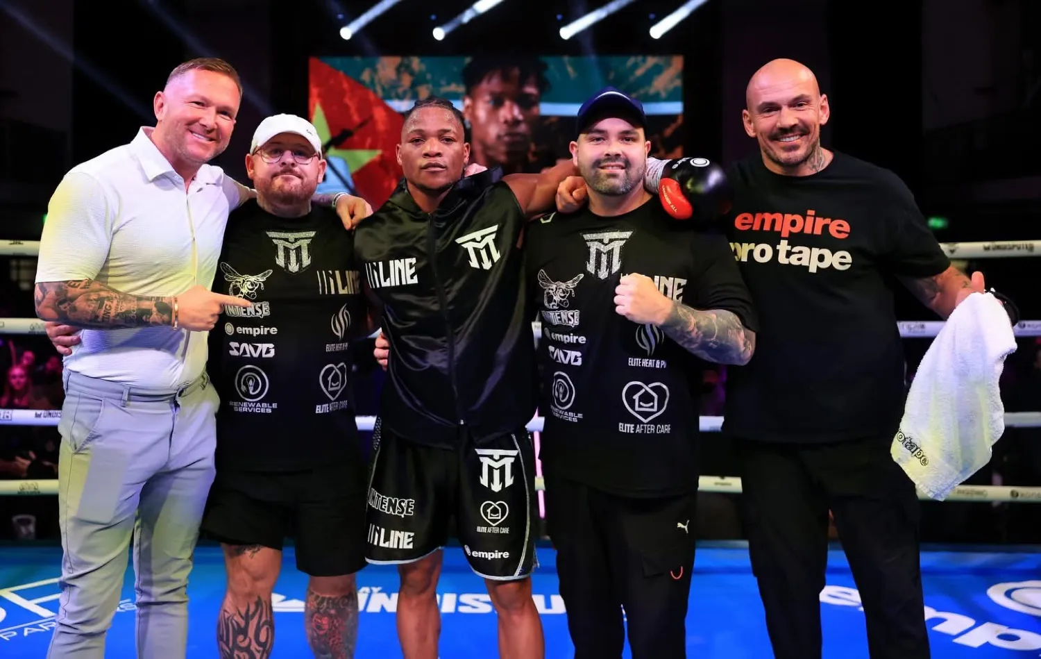 The team in the ring with a boxer in a black Iline kit after a win