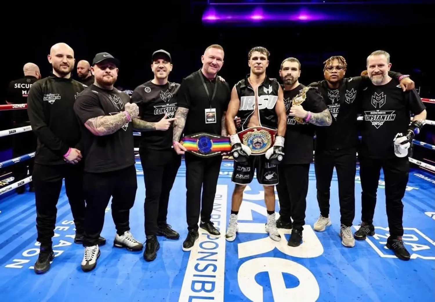 Constantin Ursu holding two championship belts with the team in a DAZN ring