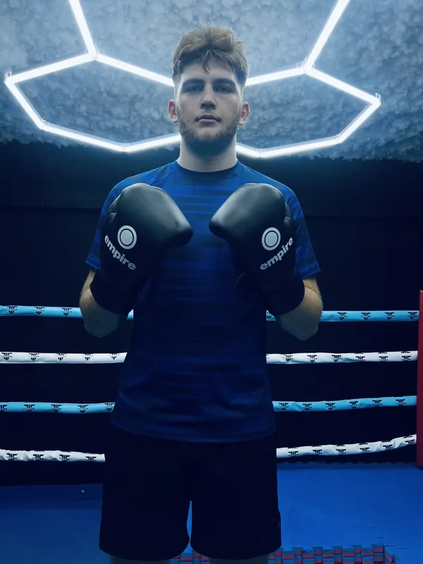 Slen Hughes in a blue top and gloves under hexagon gym lights