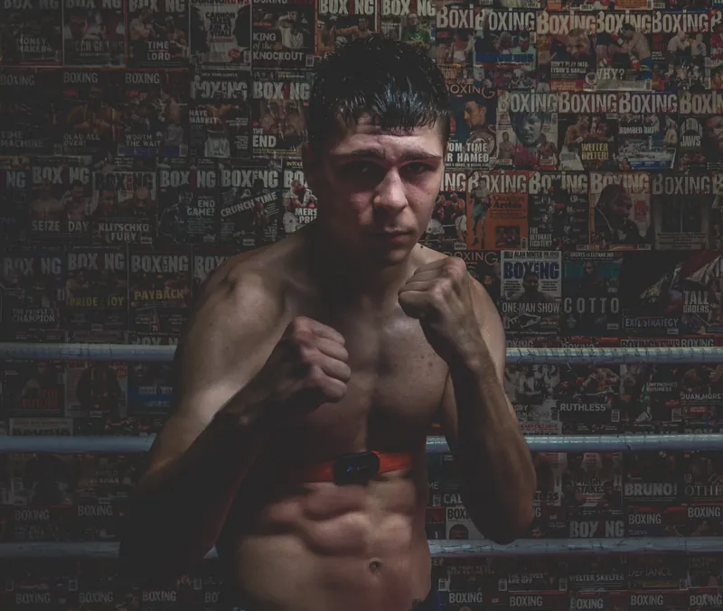 Constantin Ursu in the ring with his guard up, in front of a wall of boxing magazine covers