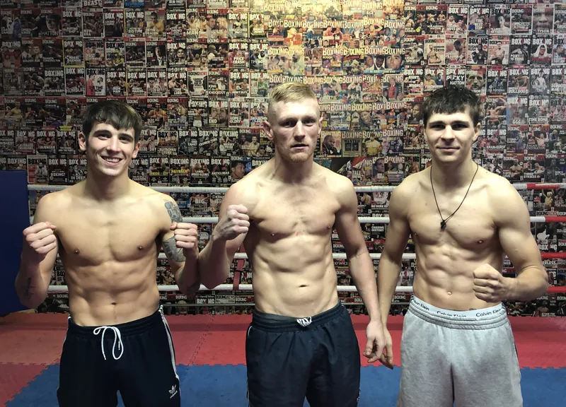 Connor Adaway, Lewis Everson and Constantin Ursu posing shirtless in front of a wall of boxing magazines