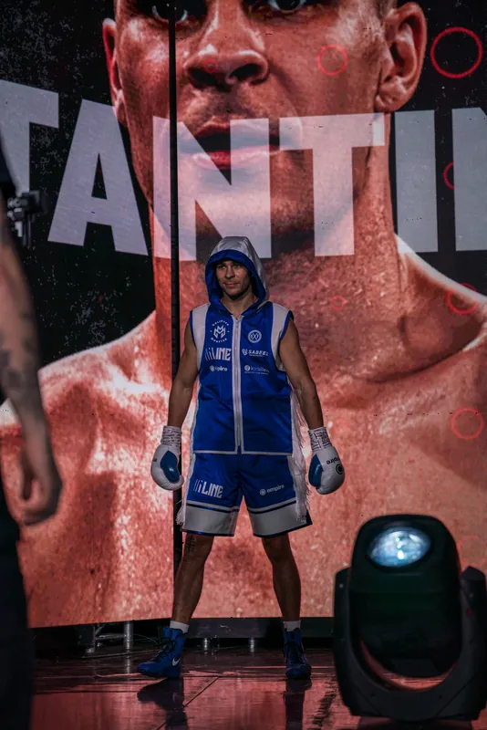 Constantin Ursu on a ring walk in a blue robe in front of a giant screen showing his name